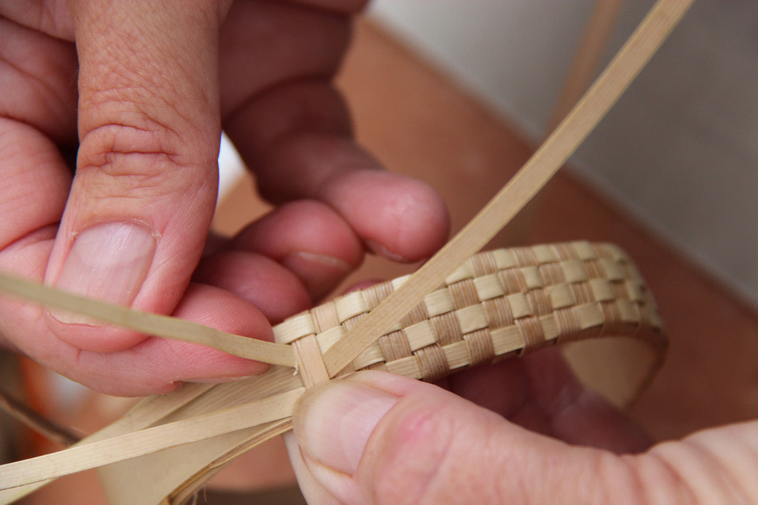 Close-up of hands weaving strips of hala leaf into a lauhala bracelet in Hawaiʻi