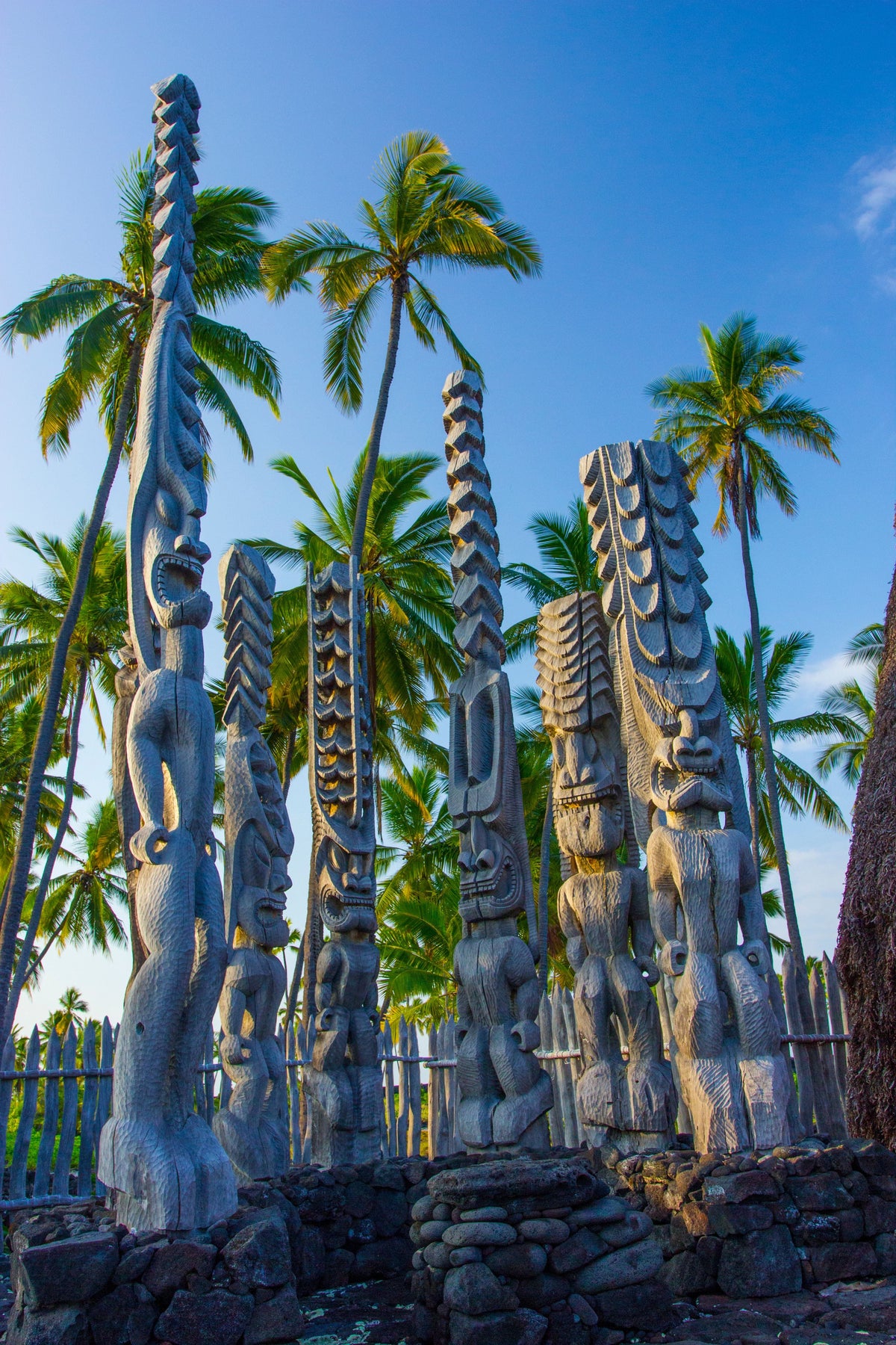 Kiʻi carved images stand among palm trees at Puʻuhonua O Hōnaunau, Hawaiʻi Island