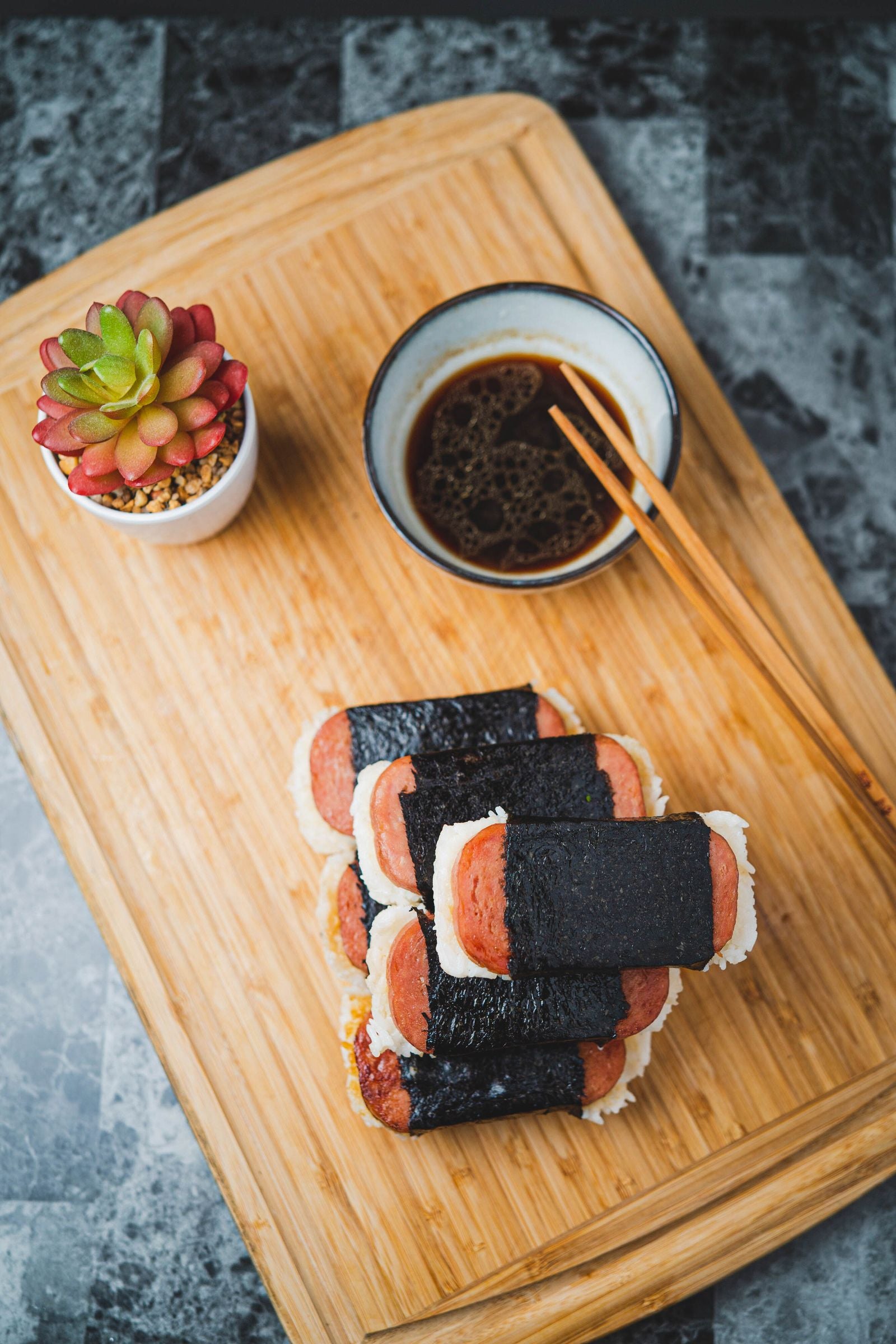 A stack of Spam musubi — grilled Spam on rice wrapped in nori — with shoyu and chopsticks, a favorite snack in Hawaiʻi