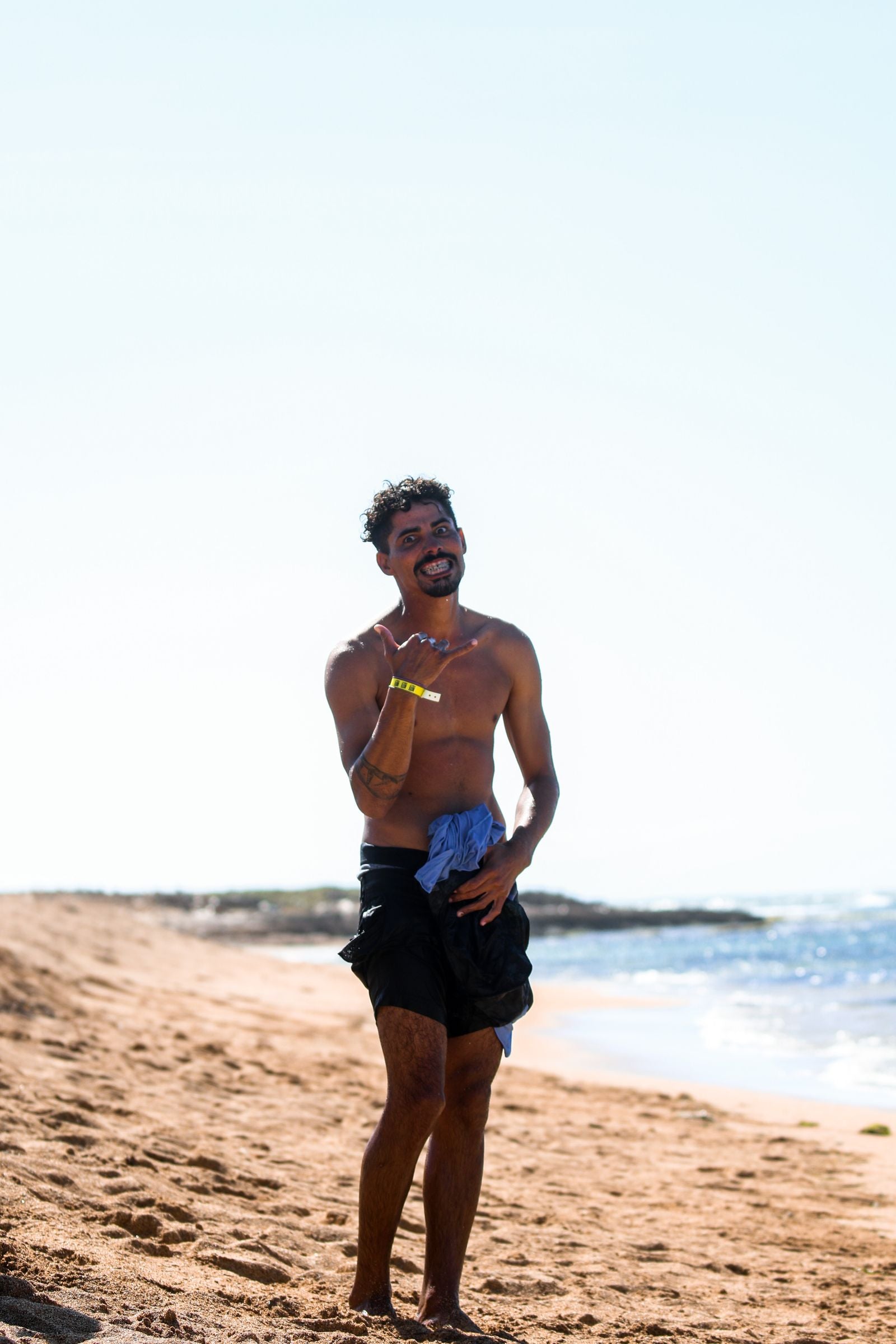 A man on a Hawaiʻi beach throwing a shaka hand sign, thumb and pinky extended, in Hawaiʻi