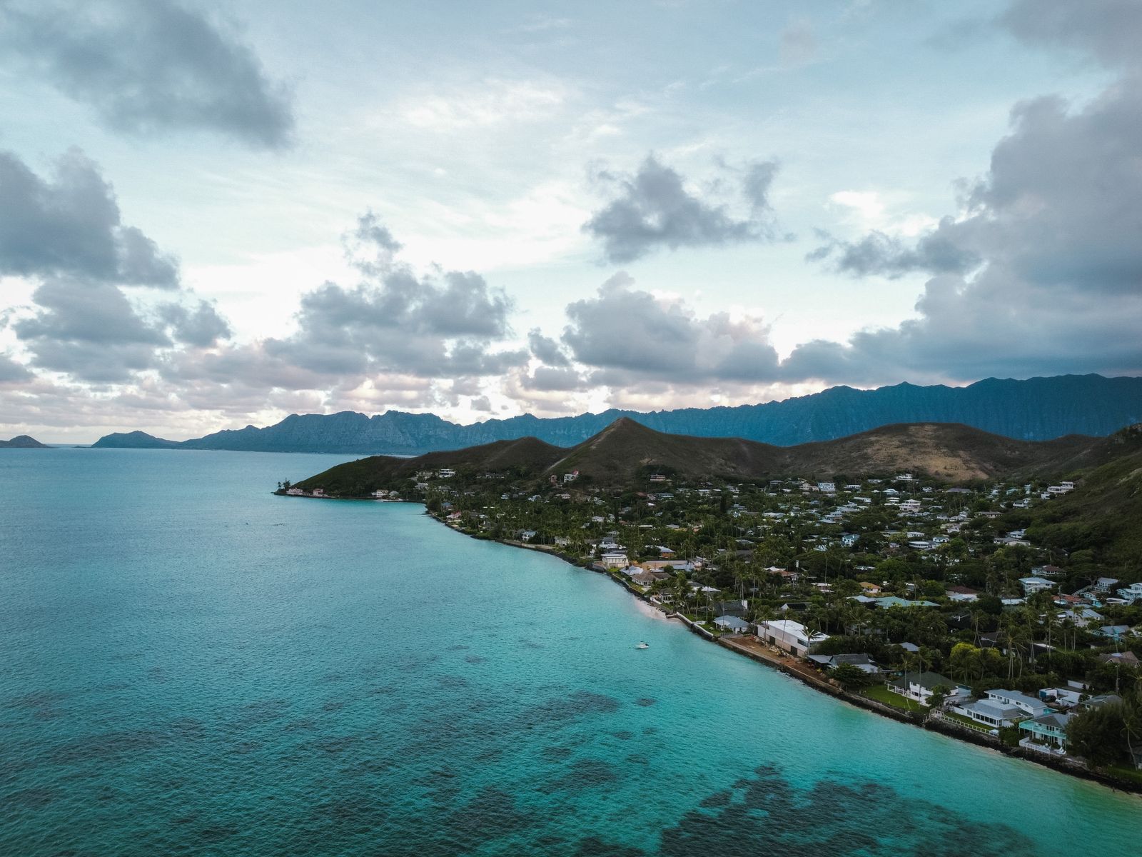 Aerial view of a turquoise Hawaiian coastline with mountains, showing the kind of island scenery travelers weigh when deciding which Hawaiian island to visit