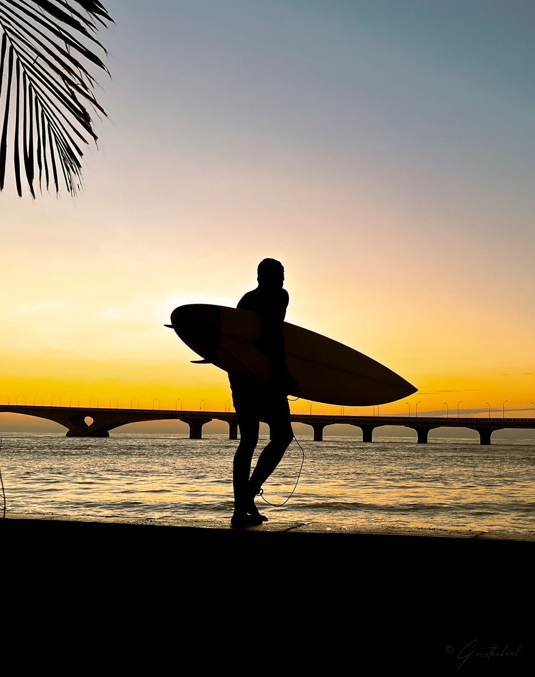 A surfer carrying a board at sunset in Hawaiʻi