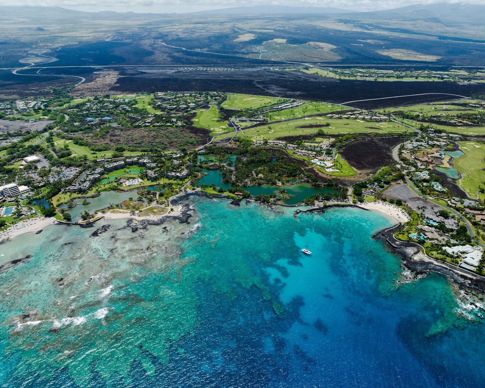 Aerial view of a turquoise Hawaiian coastline, lava fields, and coastal resorts on Hawaiʻi Island