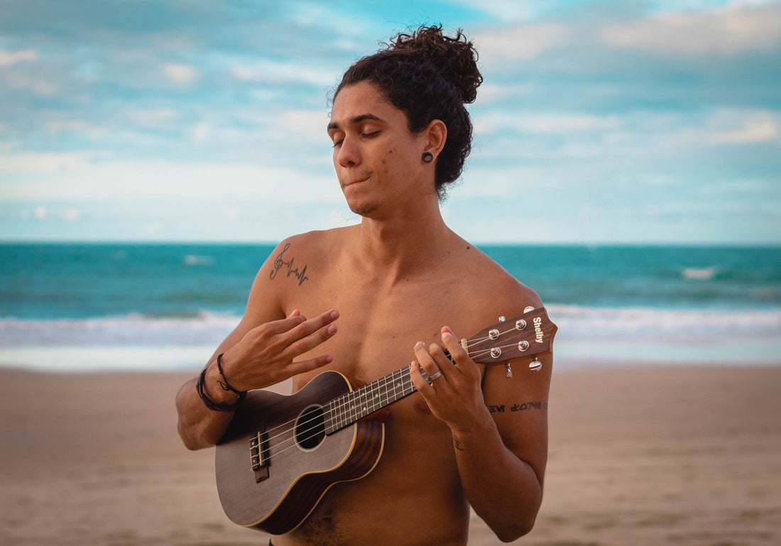 A musician playing a ukulele on a beach beside the ocean, the instrument at the heart of Hawaiʻi's musical tradition
