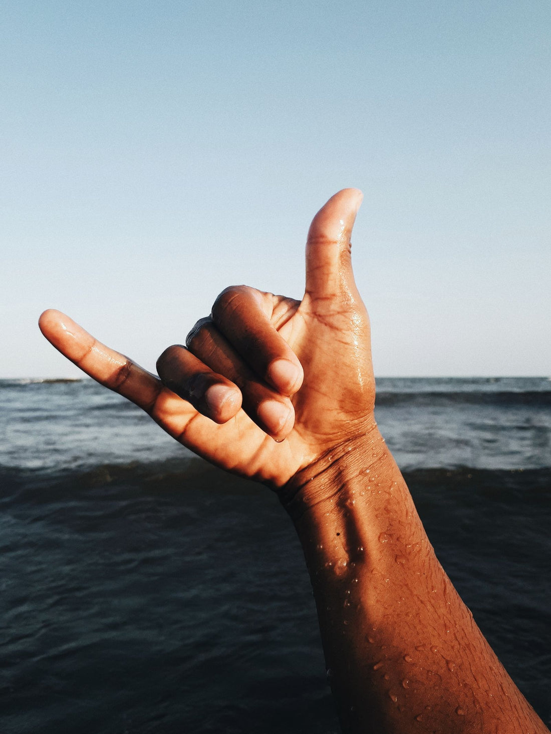 A hand making the shaka sign over the ocean in Hawaiʻi