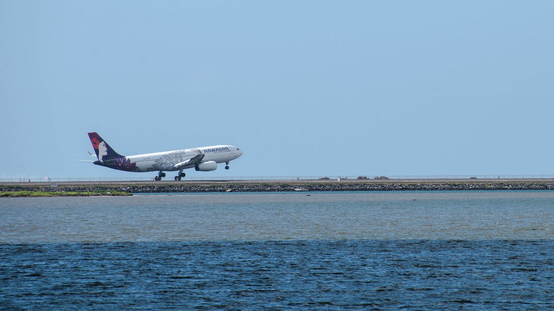 A Hawaiian Airlines jet taking off over the water near a Hawaiʻi airport runway