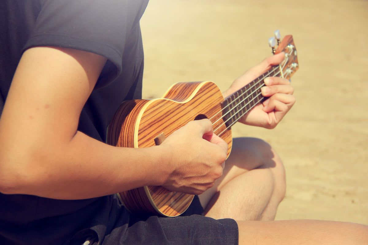 Close-up of hands playing a ukulele on a sandy Hawaiian beach