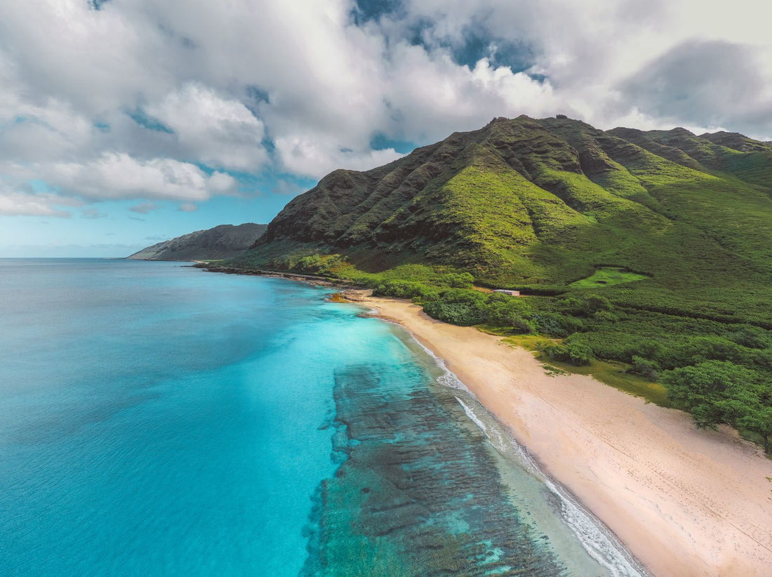 Aerial view of a turquoise Hawaiian coastline with a sandy beach and green mountains, Hawaiʻi