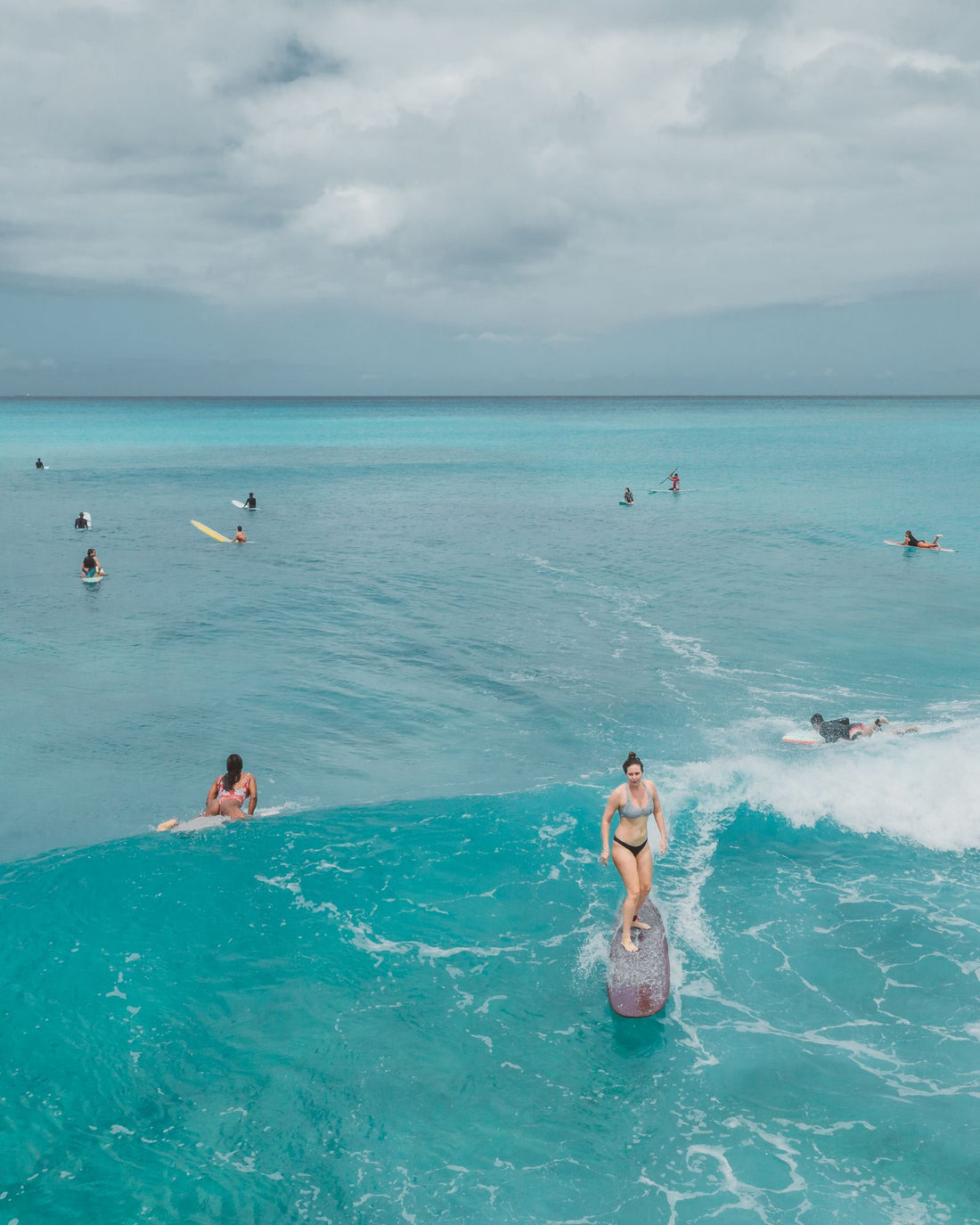 A surfer riding a longboard on a turquoise wave with other surfers in the lineup, Hawaiʻi
