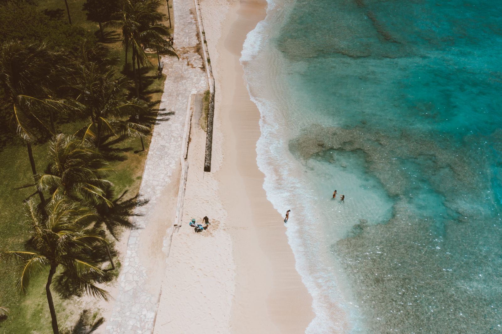 Aerial view of a palm-lined white-sand Hawaiian beach with turquoise reef water