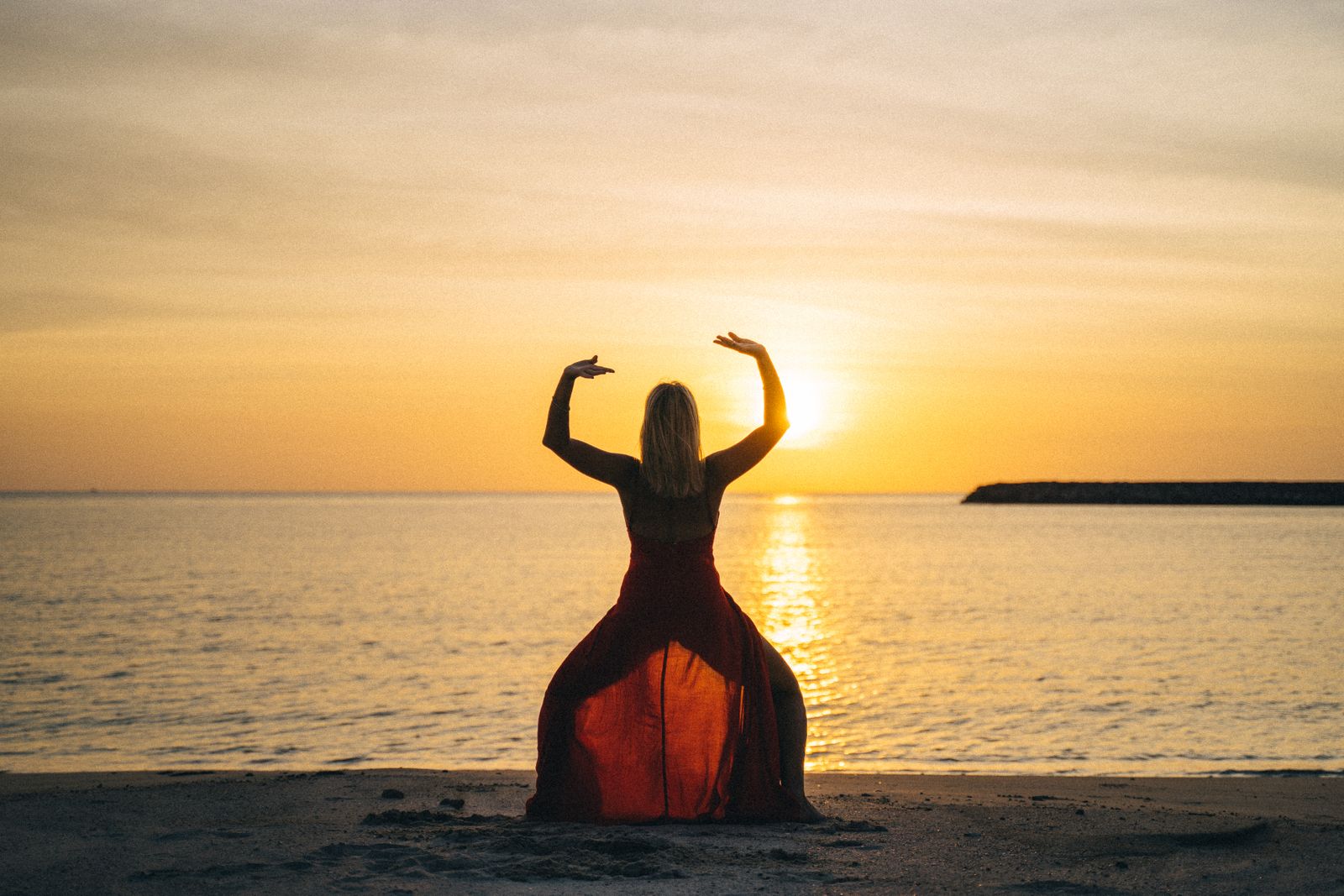 Woman in a serene pose on the beach at sunset over the ocean, finding an aloha state of mind in Hawaiʻi