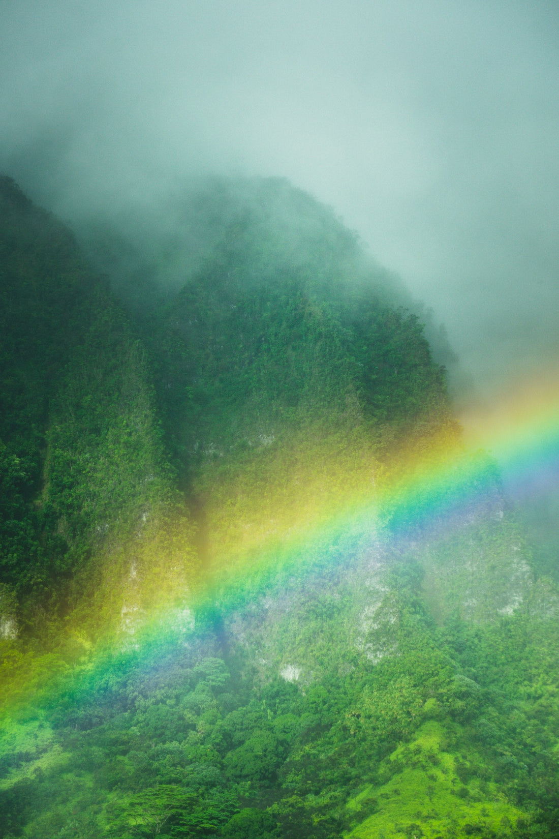A rainbow (ānuenue) arcs across the misty green mountains of Hawaiʻi
