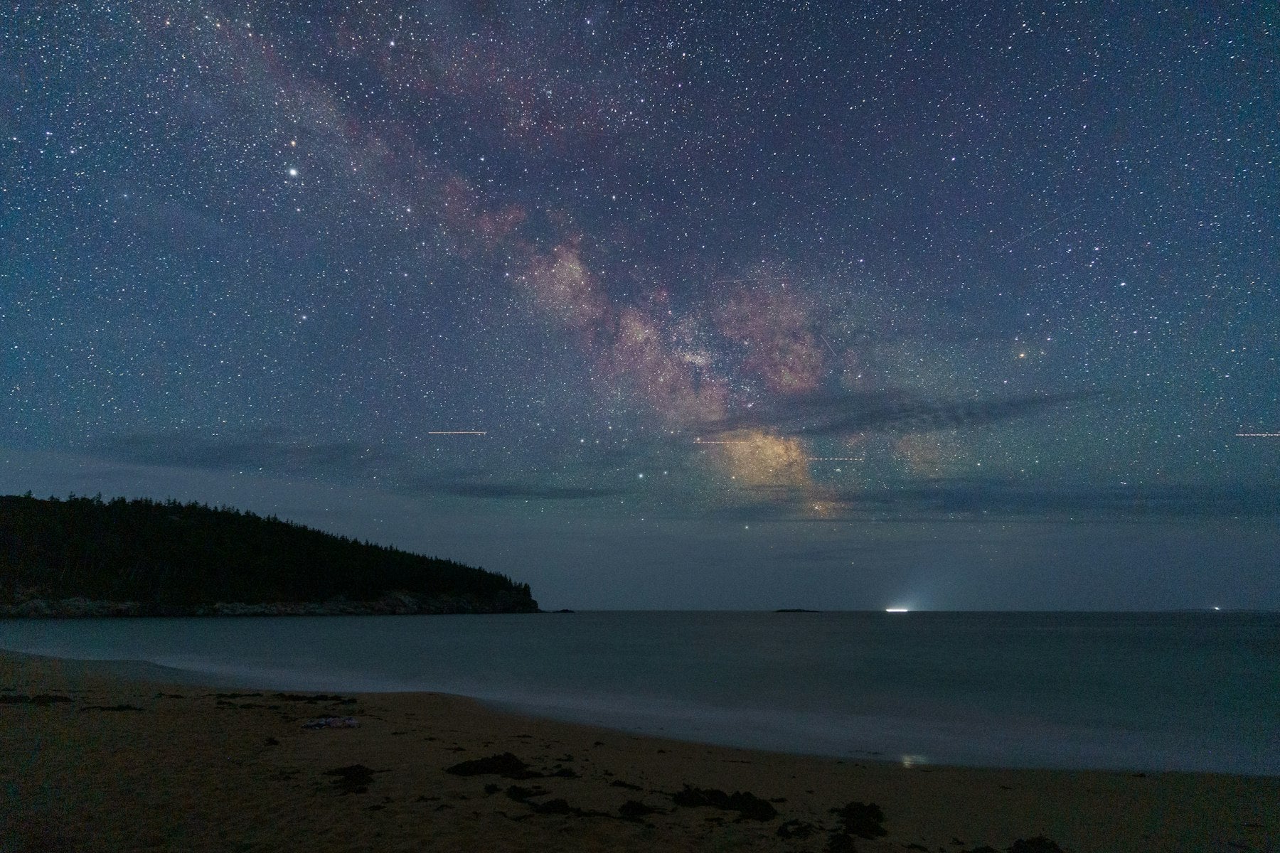 The Milky Way arching over a dark ocean beach at night, the kind of sky Hawaiian wayfinders read