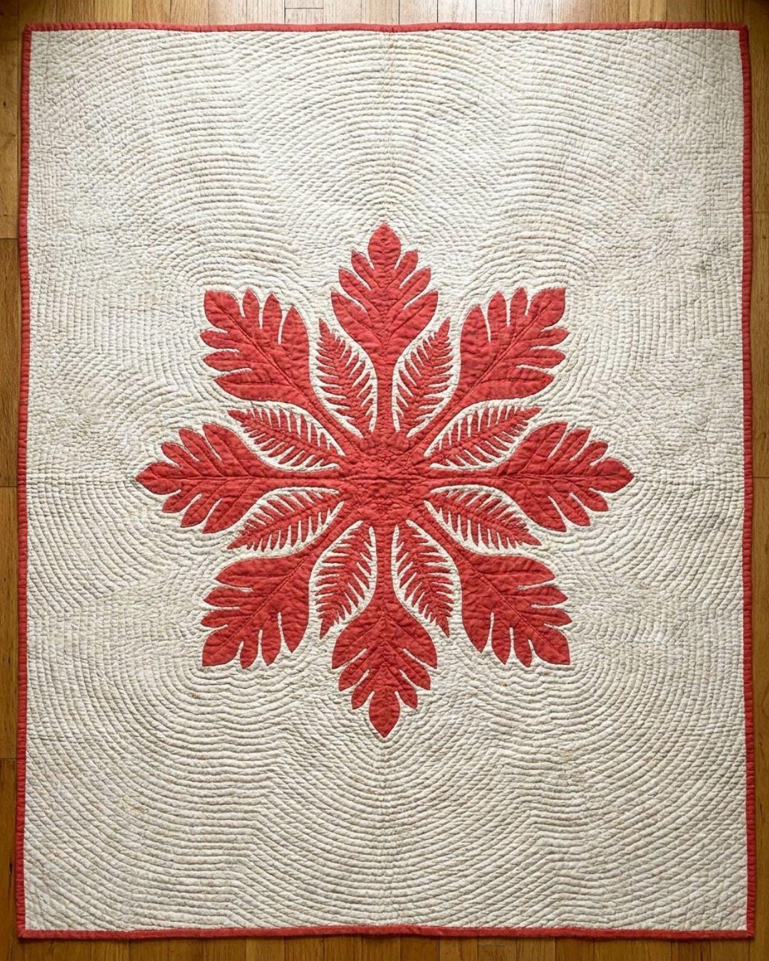 An authentic Hawaiian quilt with a single large symmetrical breadfruit-and-fern appliqué design in coral red on cream, echo-quilted in rippling lines